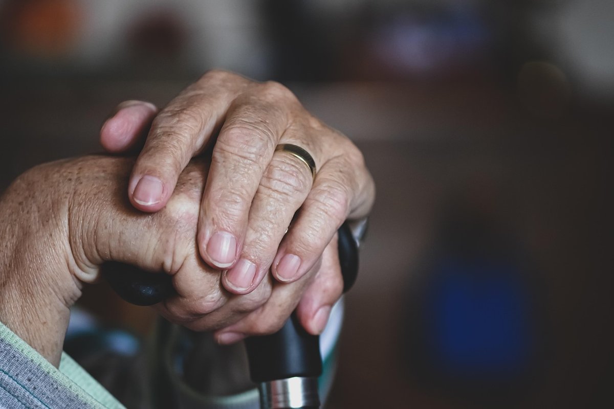 Close up of an elderly person's wrinkled hands resting on the handle of a walking cane